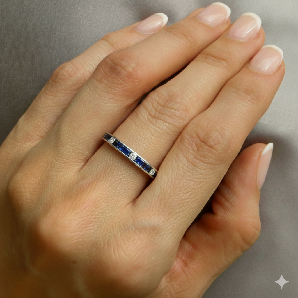 Close-up of a hand wearing a ring with blue stones on a neutral background